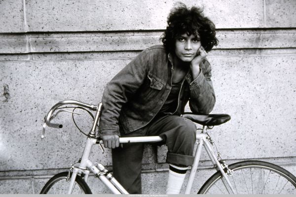 Image of a teenaged boy holding a bicycle with one  leg draped over it and facing the  camera.