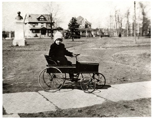 Image of a boy in black coat in a child's wagon looking at the screen.