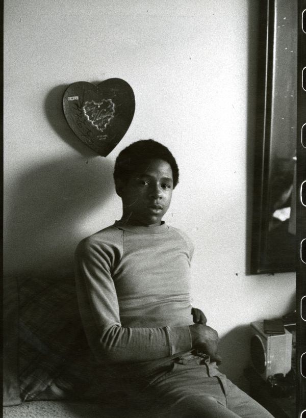 Image of a teenaged boy looking at the camera on his bed in a group home.