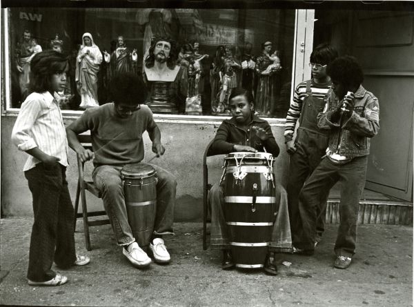 Image of several young people gathered outside a Santería, playing percussion instruments.