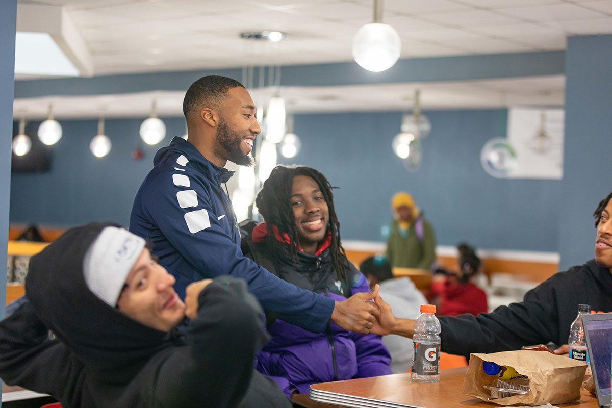A group of students smiling and greeting each other with a handshake in Underground Lounge Café.