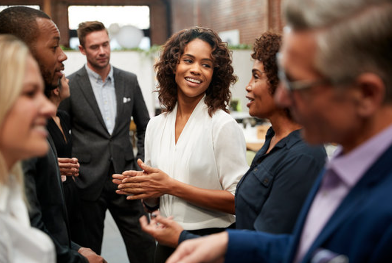 A diverse group of professionally dressed people smiling and engaging in conversation at a networking event in an open office space