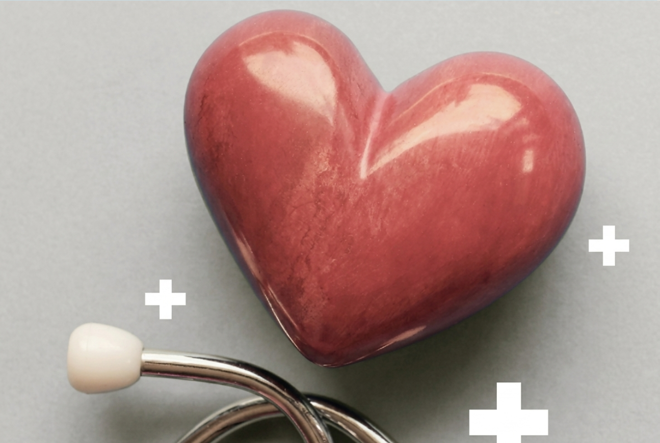 A polished, heart-shaped red stone resting above the metal earpieces of a stethoscope, accented by small white cross symbols on a grey background.