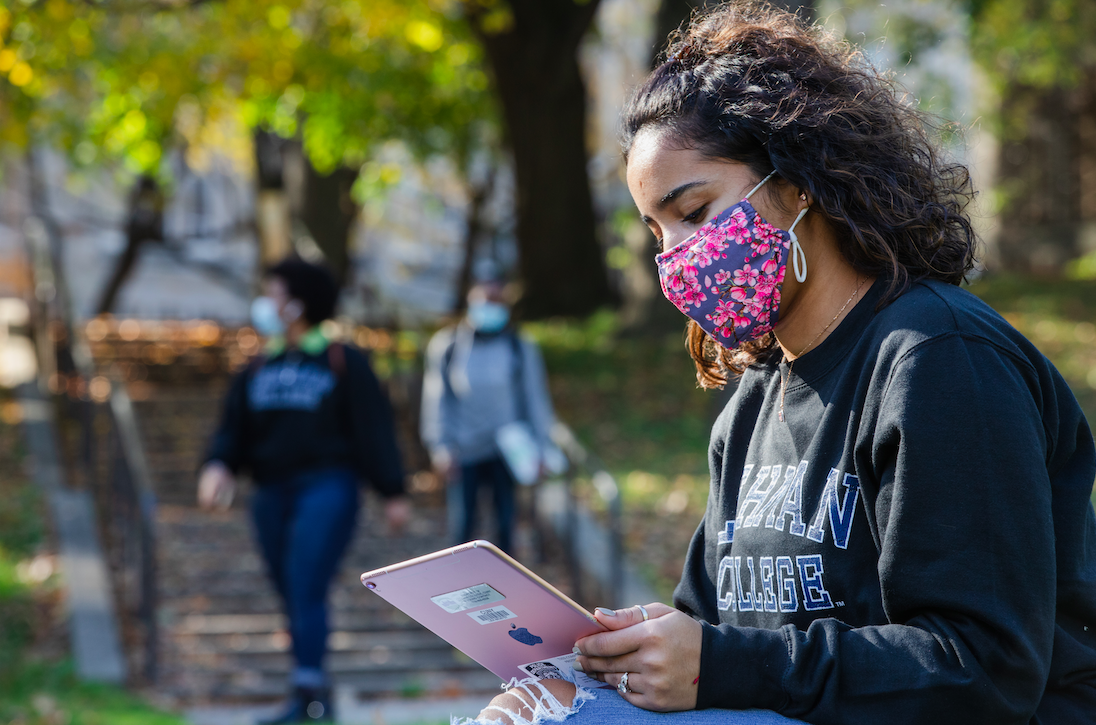 masked female student looking at an iPad.