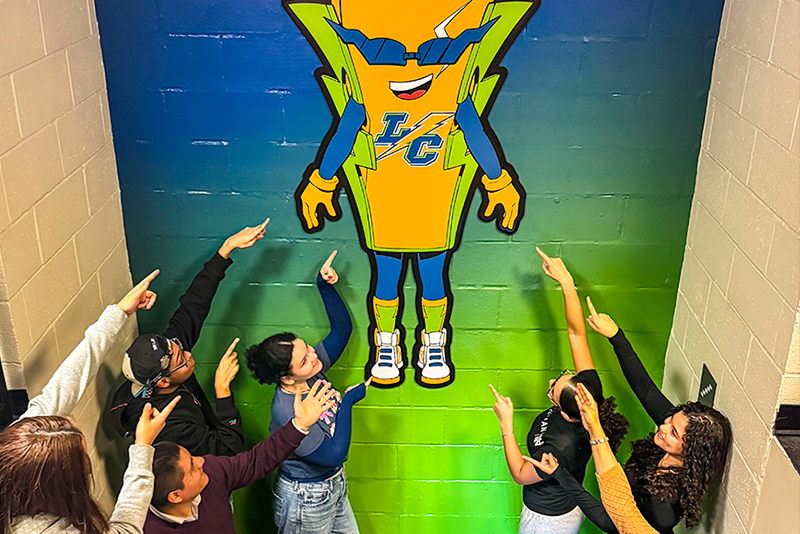 Students and Staff Point at El Rayo Mural in Student Life Building