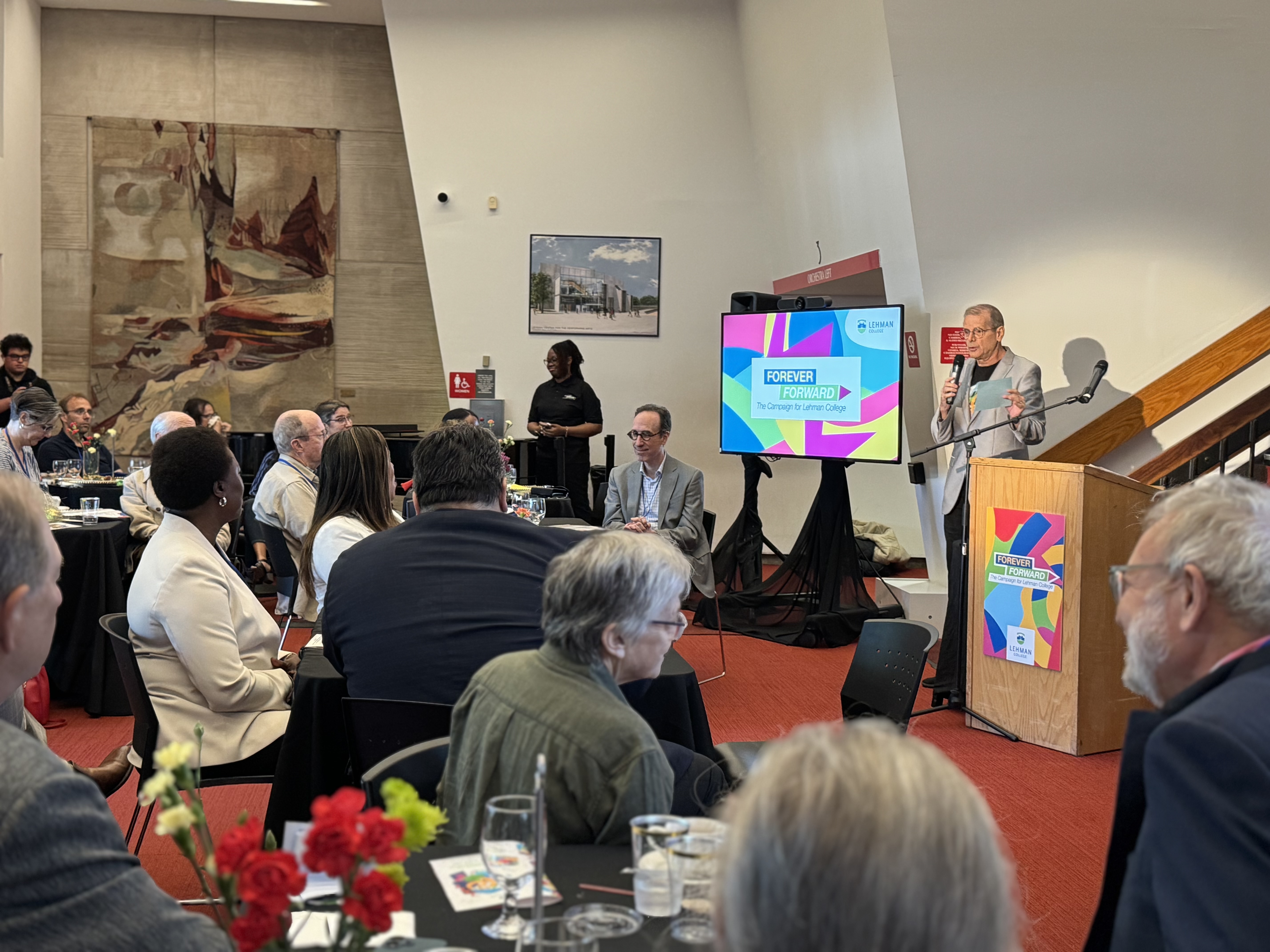 a man with a microphone addresses a sitting crowd.