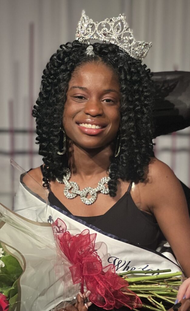 Latavia Sturdivant in her wheelchair wearing an evening gown with flowers, crown, and sash.