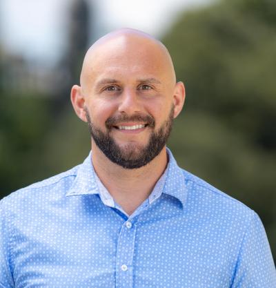 Head shot of a man with a beard, shaved head, and blue shirt.