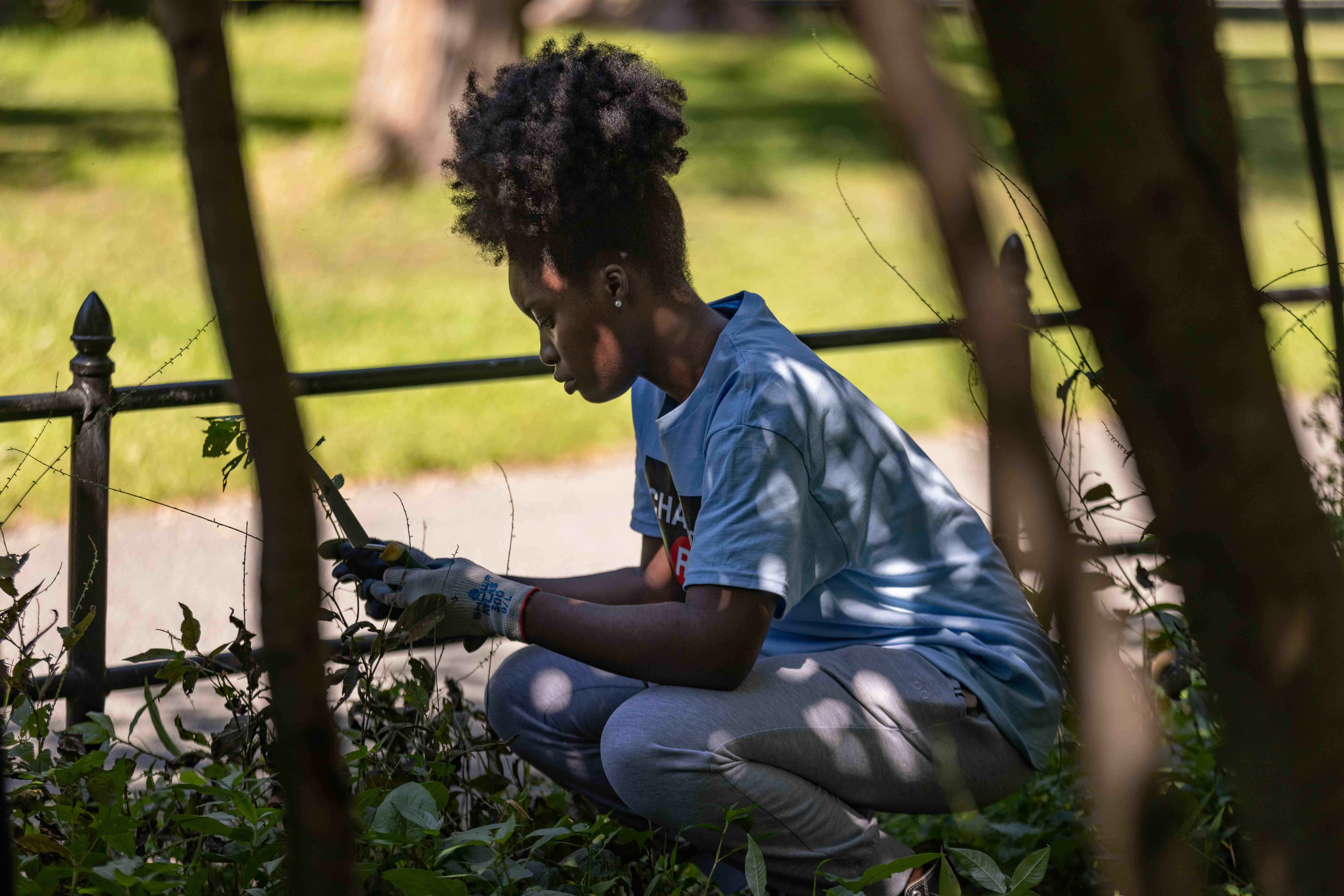A young woman crouching while clearing vegetation from a burial ground of unmarked graves.
