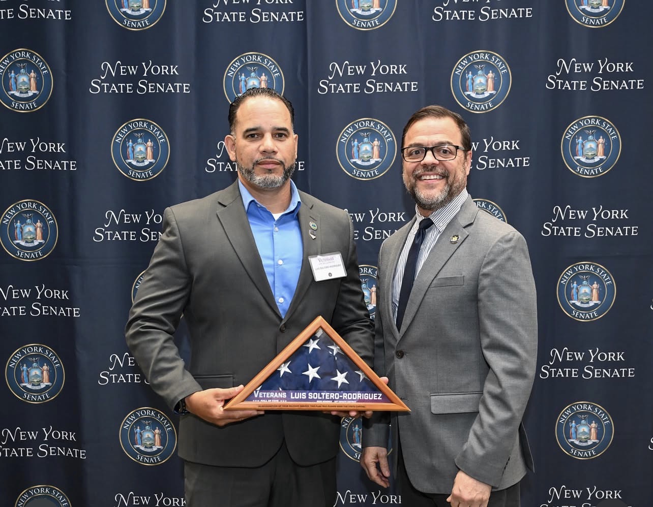 Luis Soltero-Rodriguez holds a folded American Flag as he poses with Senator Luis Sepulveda.