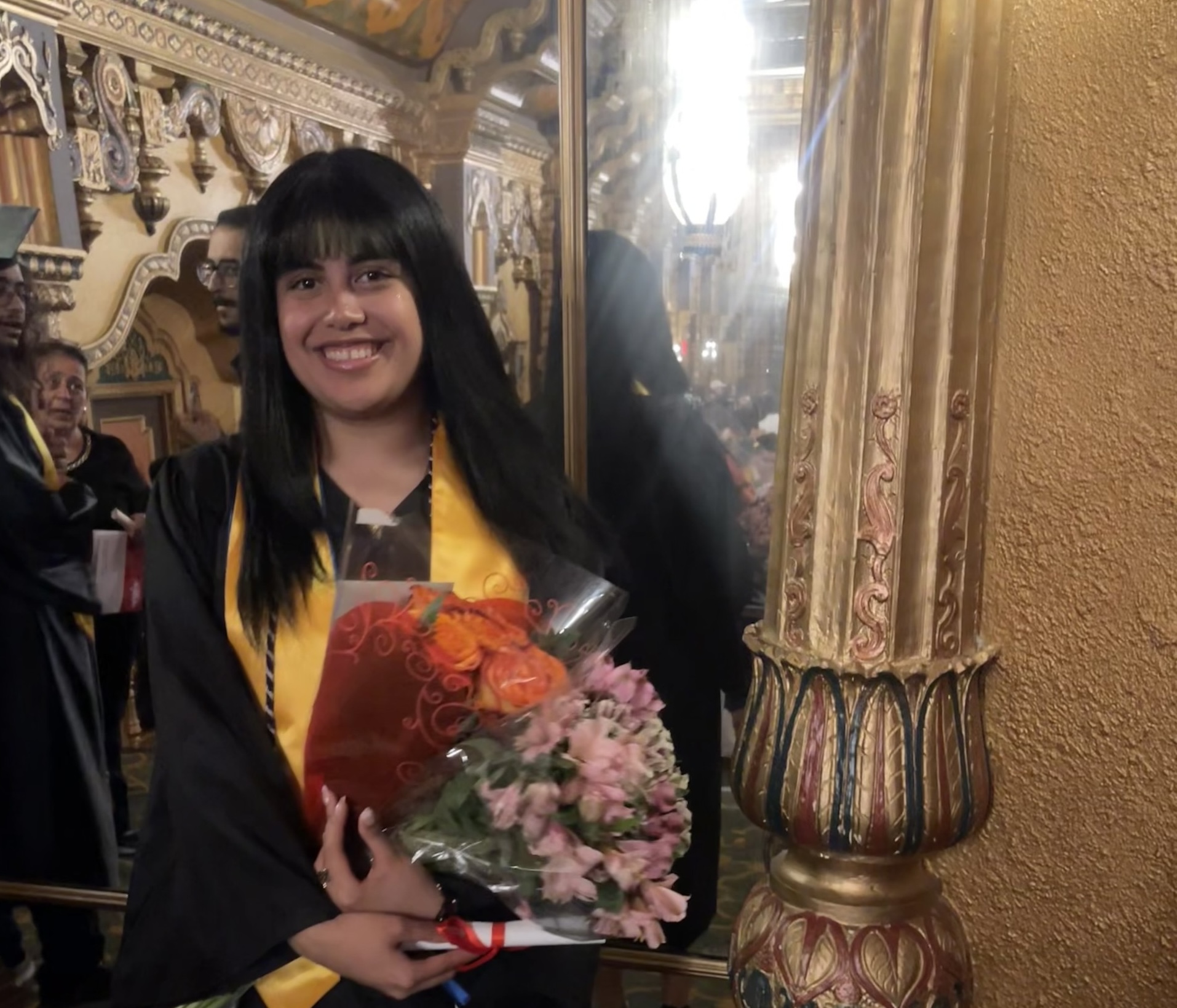 Kiara Meza in commencement regalia holds a bouquet of flowers.