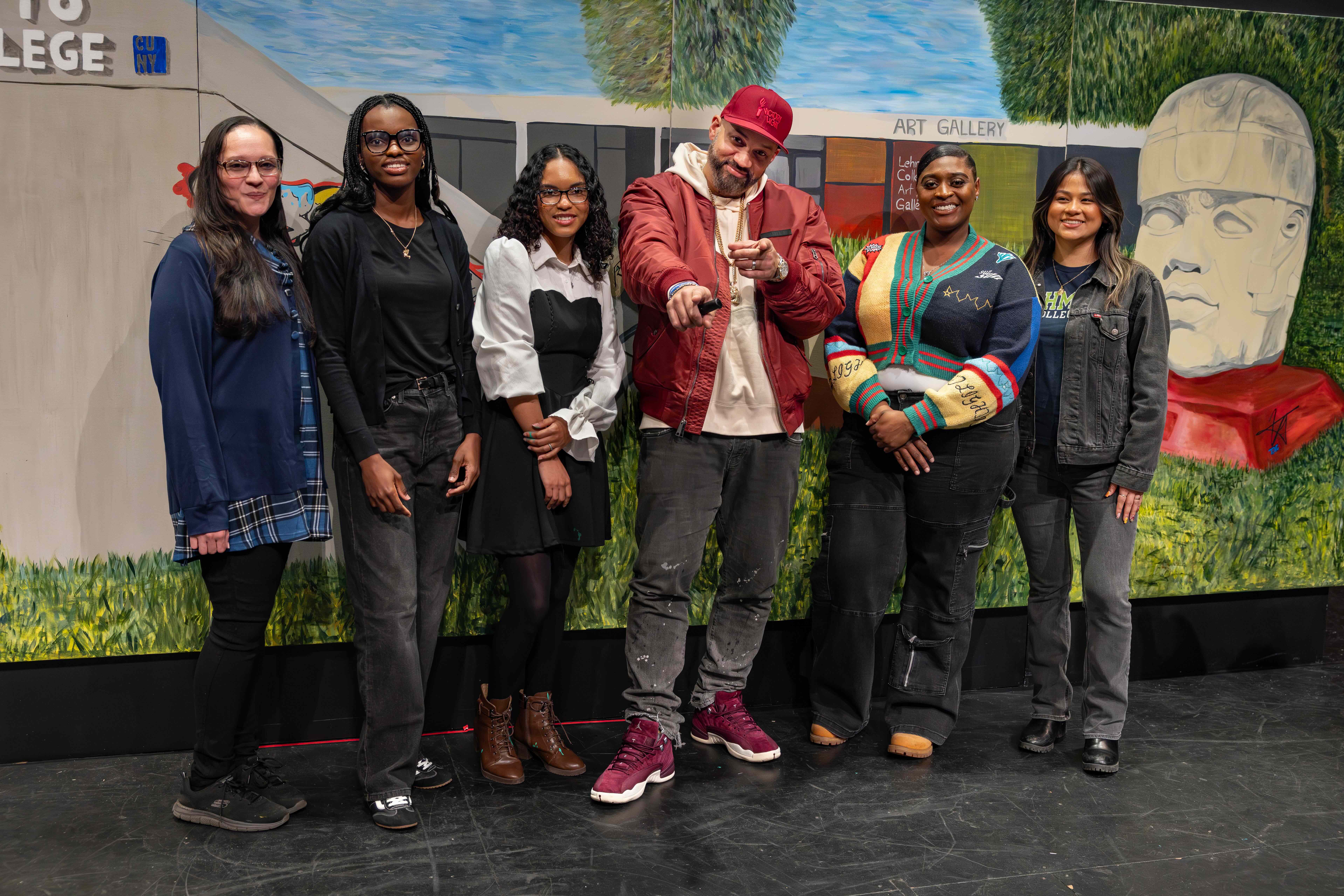 A group of art students, their professor, and The Kid Hero pose in front of a mural