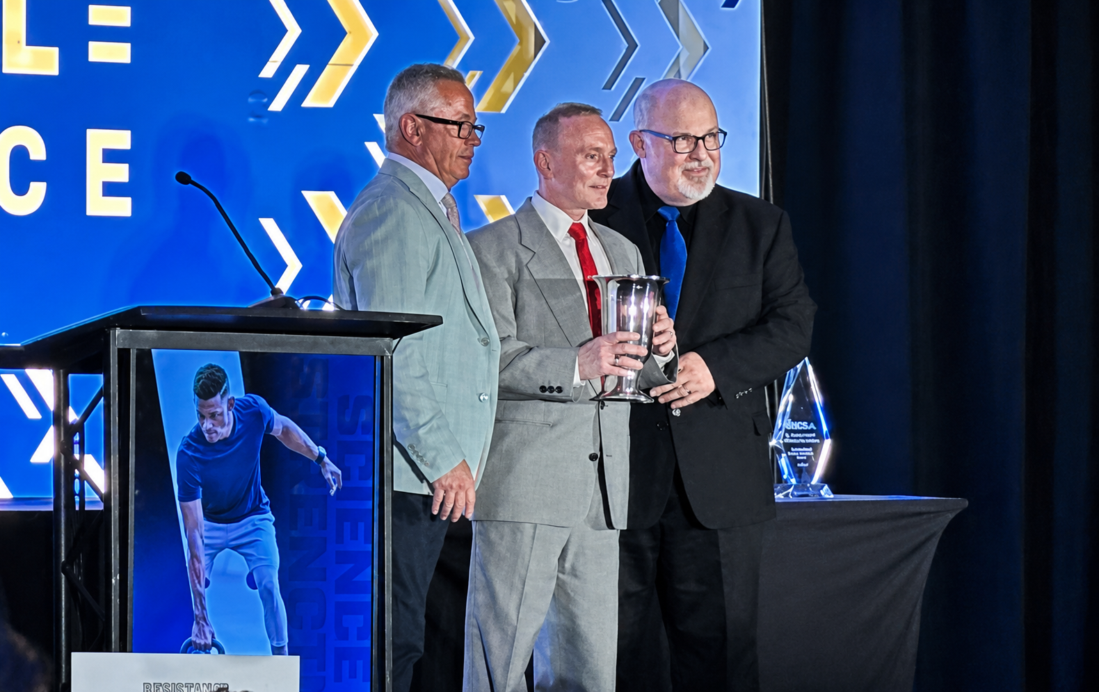 Brad Schoenfeld, center, holds an award trophy, flanked by members of the National Strength and Conditioning Association