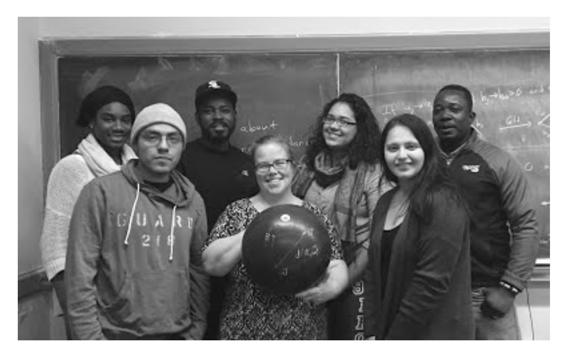 Black and white photo of Christina Sormani holding a large globe, surrounded by her students