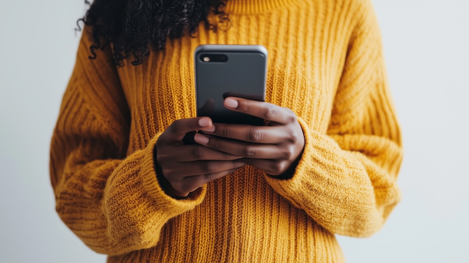 Photo from the neck down of a person in a yellow sweater looking at a phone.