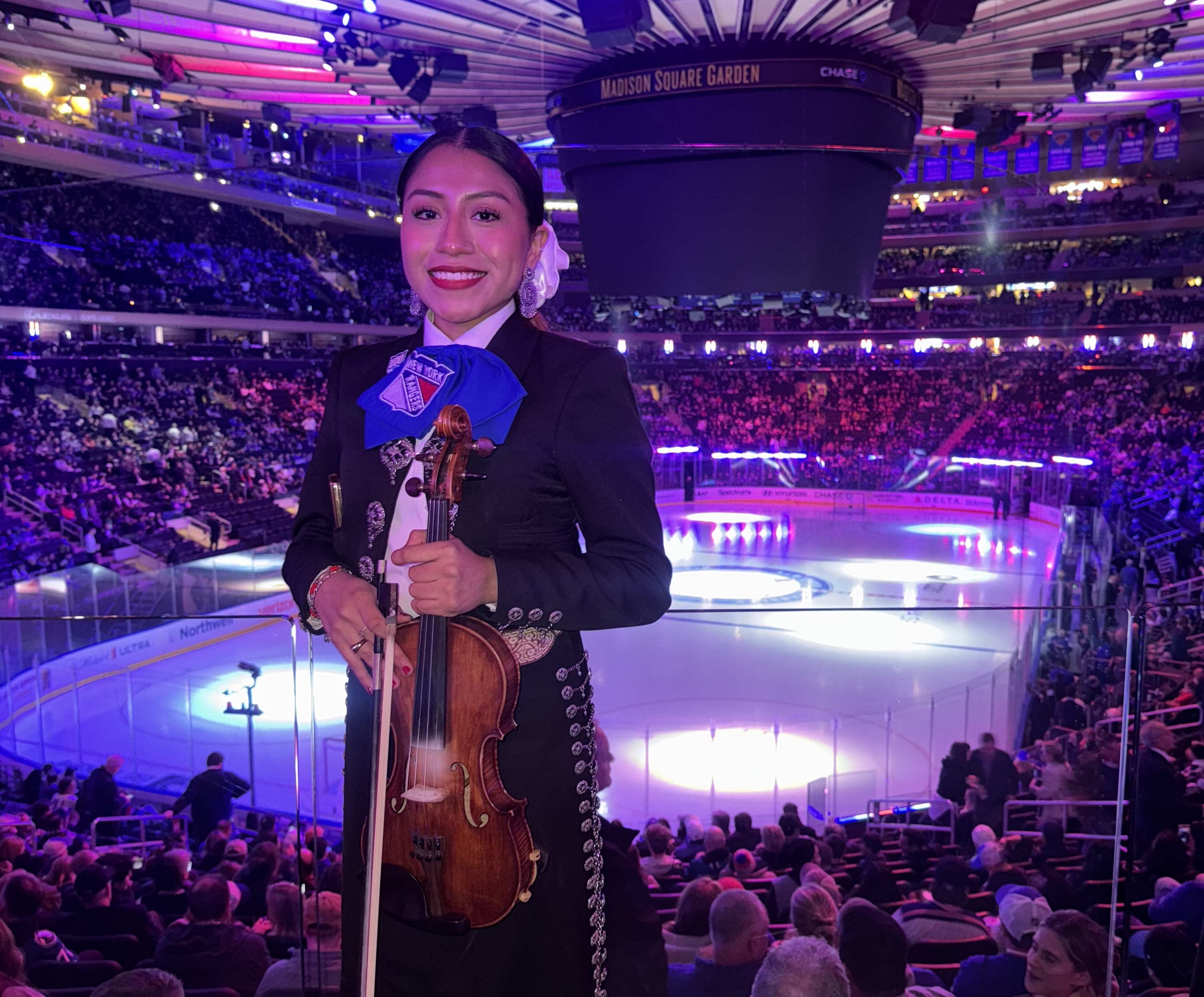 A young woman in a mariachi costume holding a violin with the arena of Madison Square Garden in the background