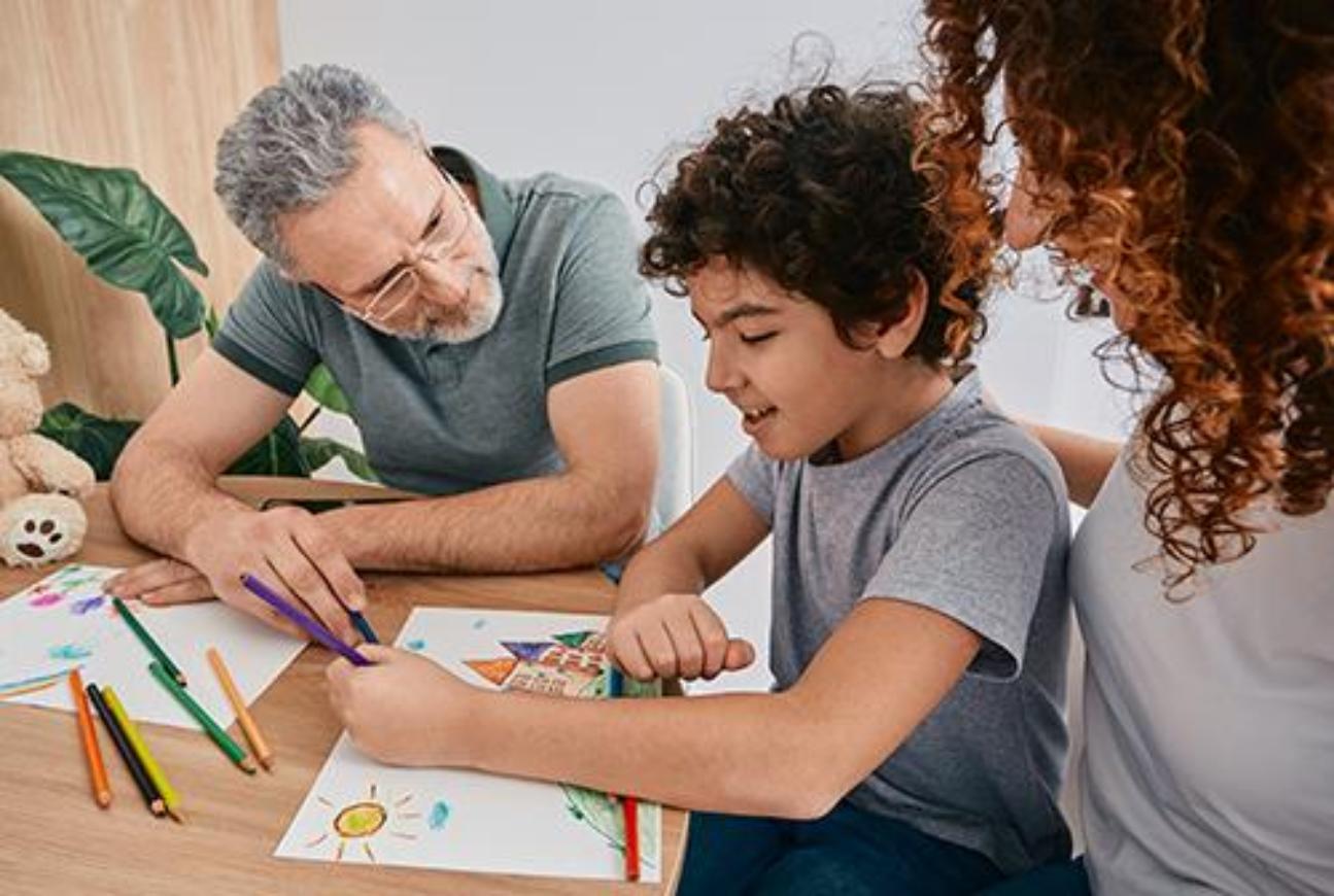 An adult and a child sitting at a table drawing with colored pencils
