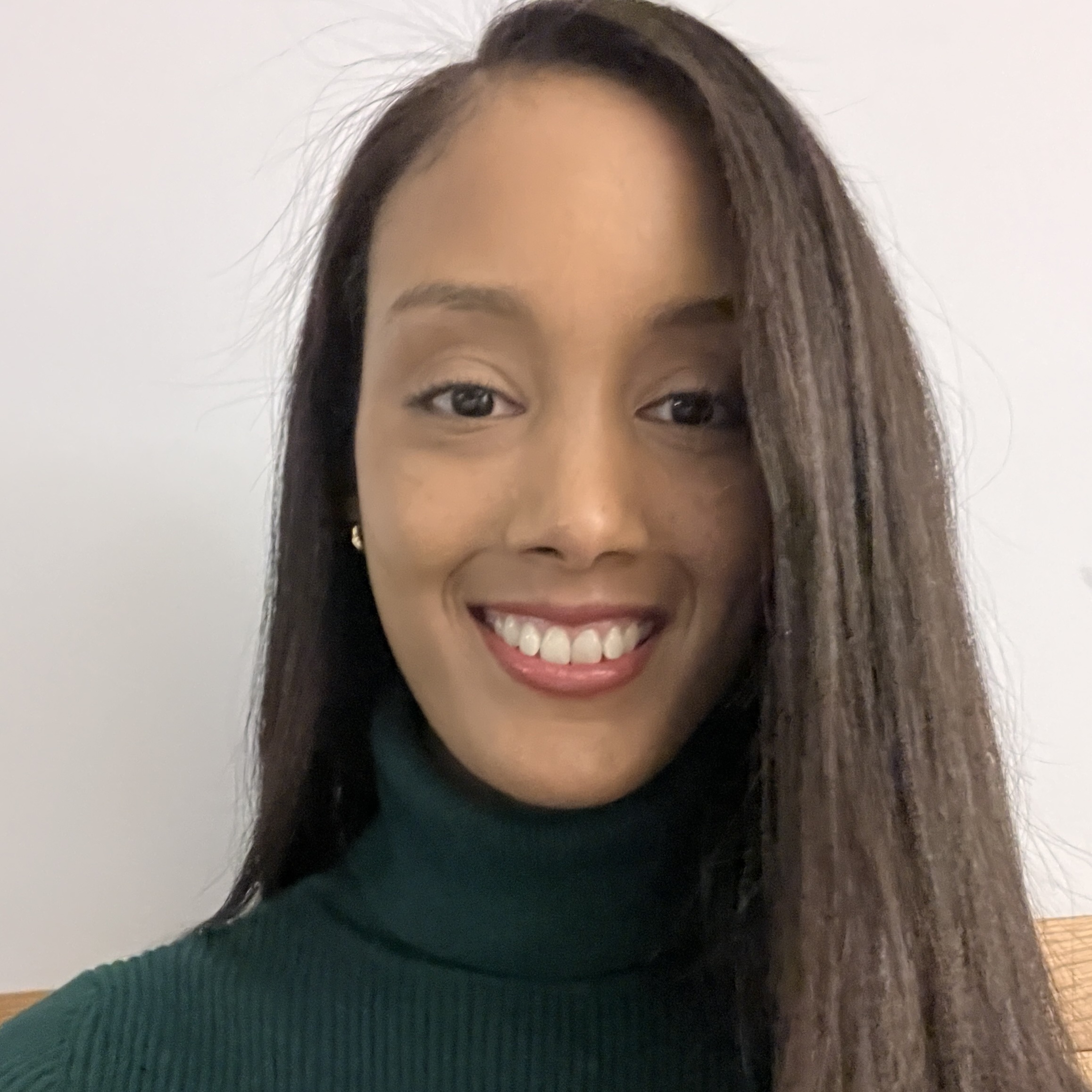 Smiling woman, with long brown hair parted on the right. Wearing a black turtle neck blouse