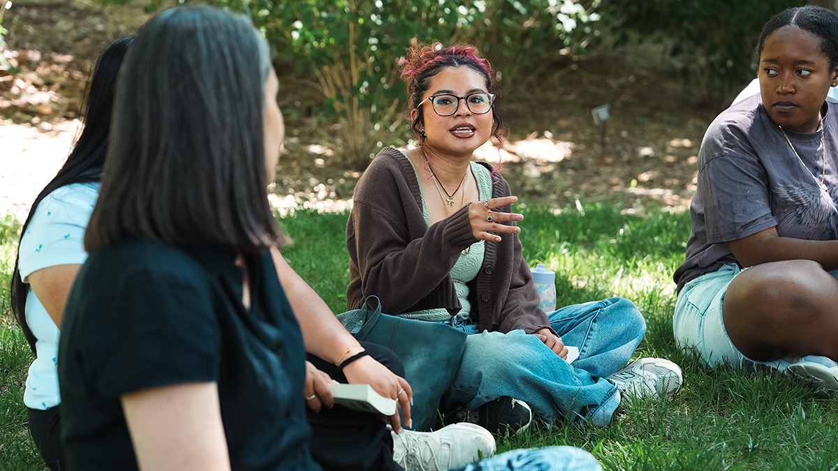 A group of students sitting outside on the grass during an informal outdoor meeting or discussion.