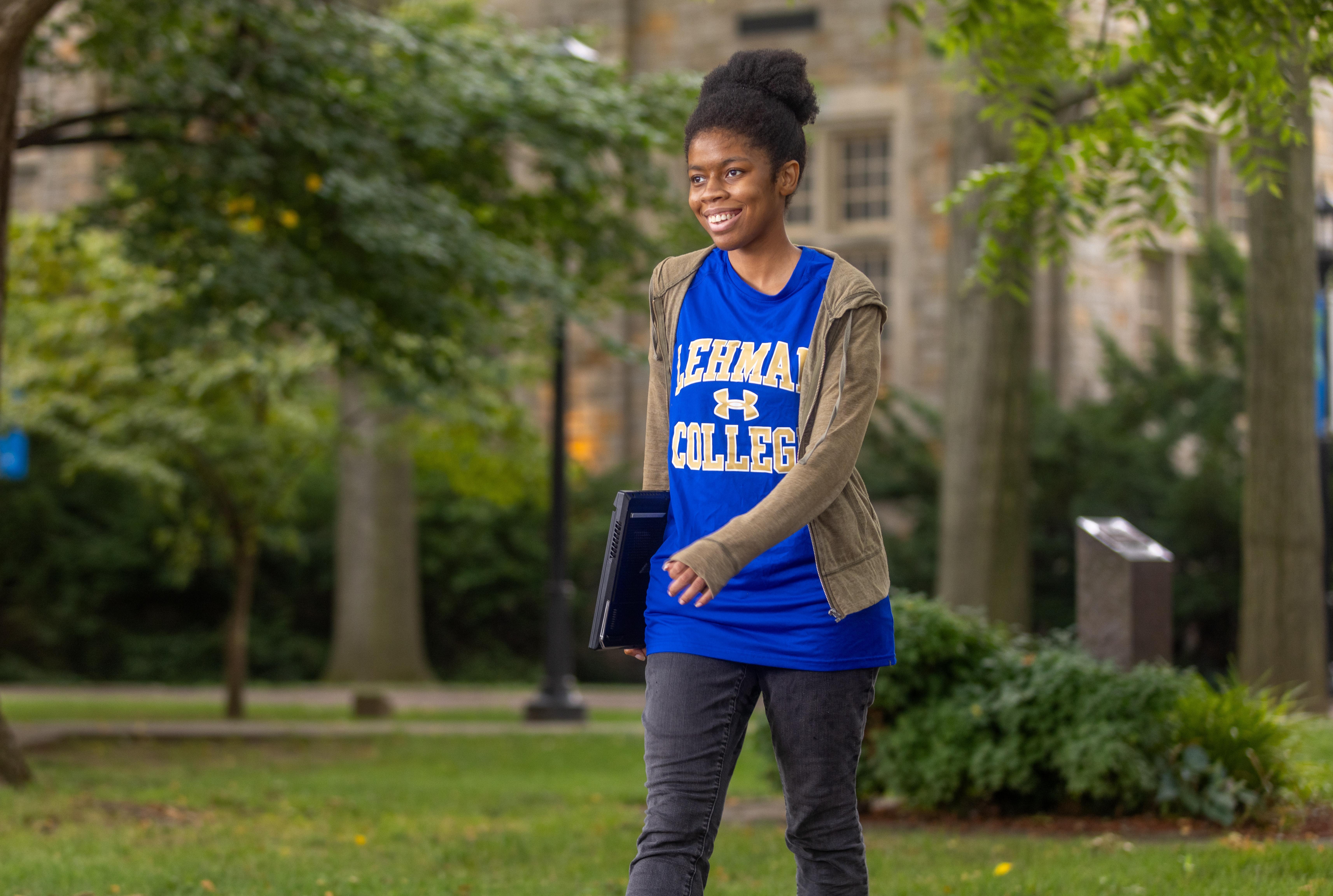 Student wearing a Lehman College shirt walking across campus