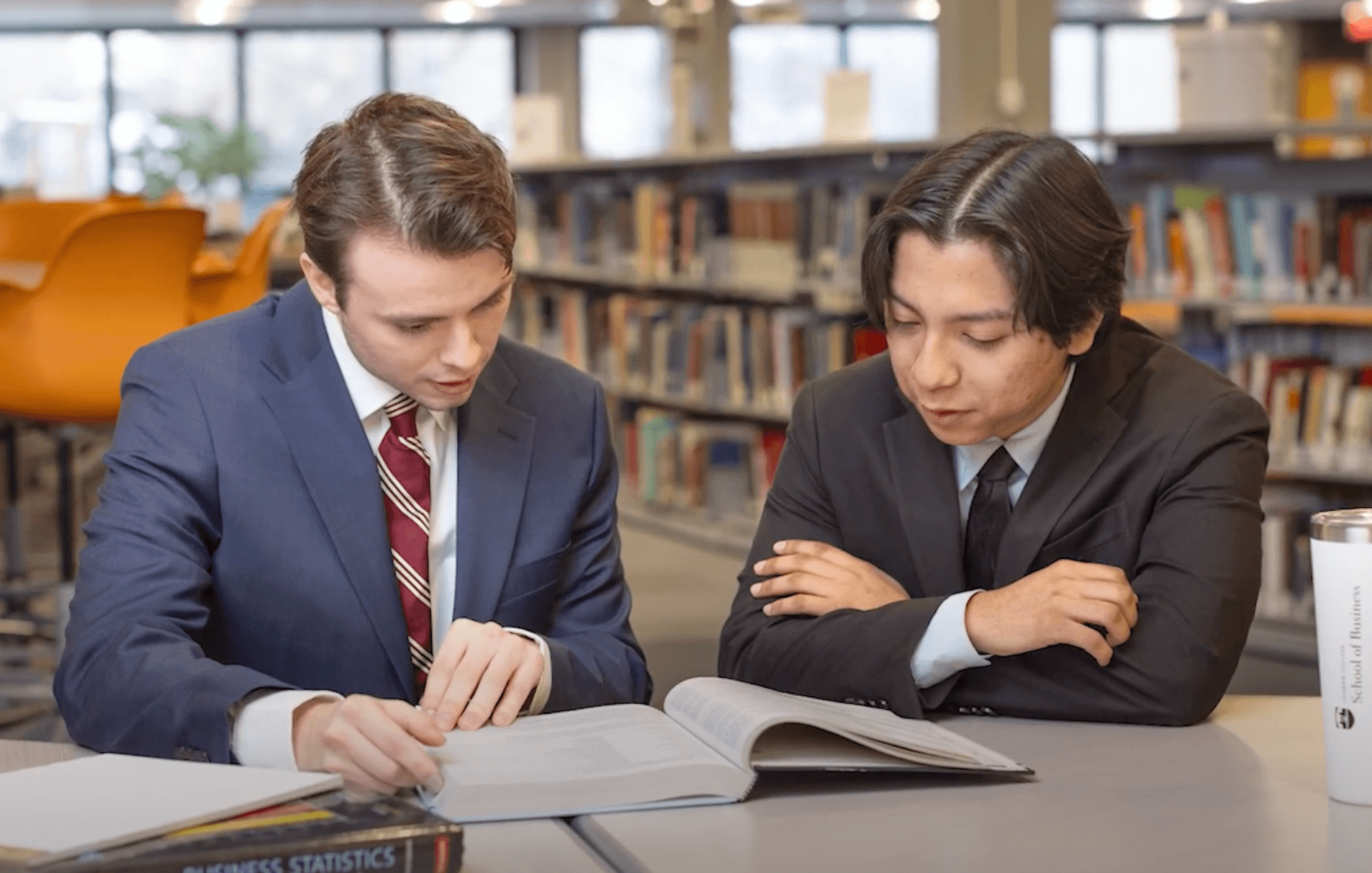 Thomas wearing a blue blazer and sitting with another student in the library